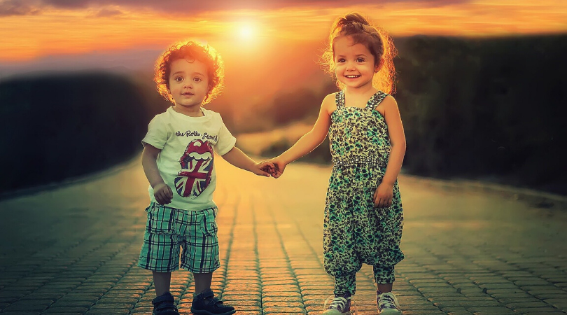 a two year old boy holding hands with a three year old girl at sunset