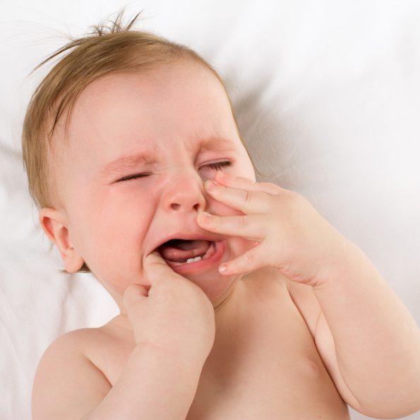 baby crying with hands in its mouth