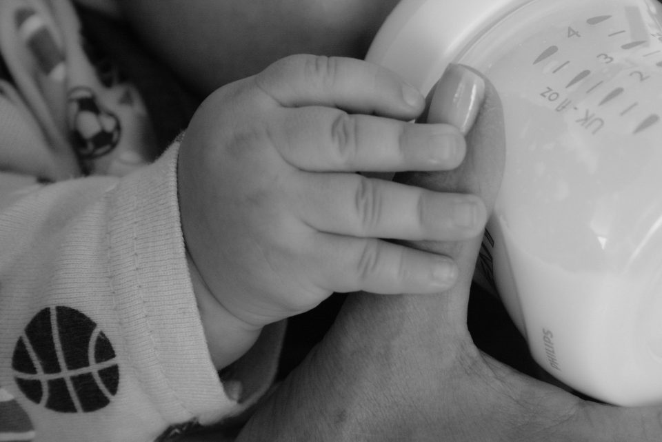 black and white photo of mums hands bottle feeding a baby