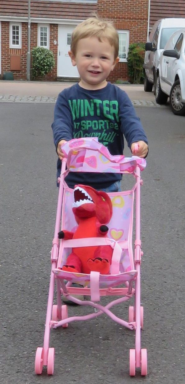 Jake pushing a T rex toy in a pink pushchair