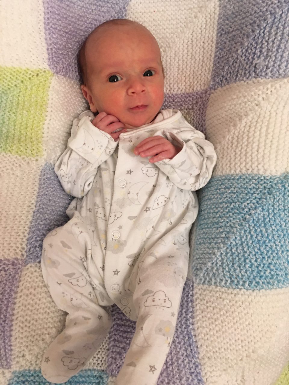 William looking very small on his due date wearing a baby gro and laying on a knitted blanket