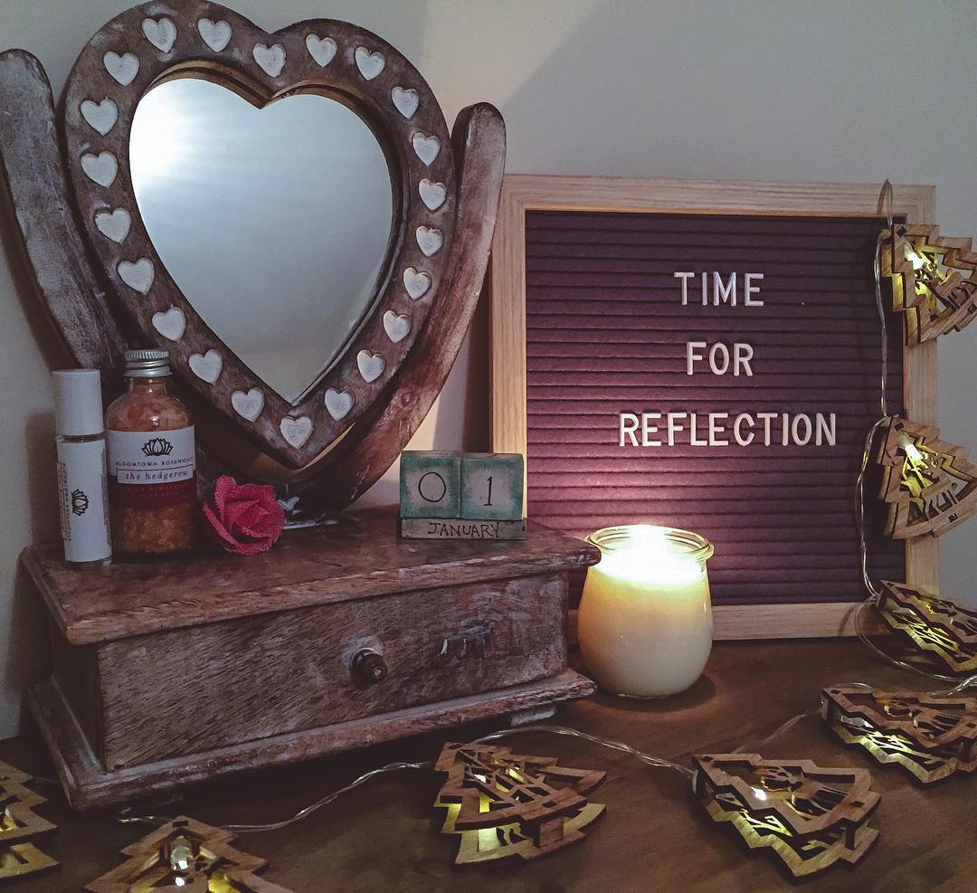 a dressing table with a heart shaped mirror and a peg board with the words time for reflection written on it. There is a lit candle and xmas tree lights draped across the surface