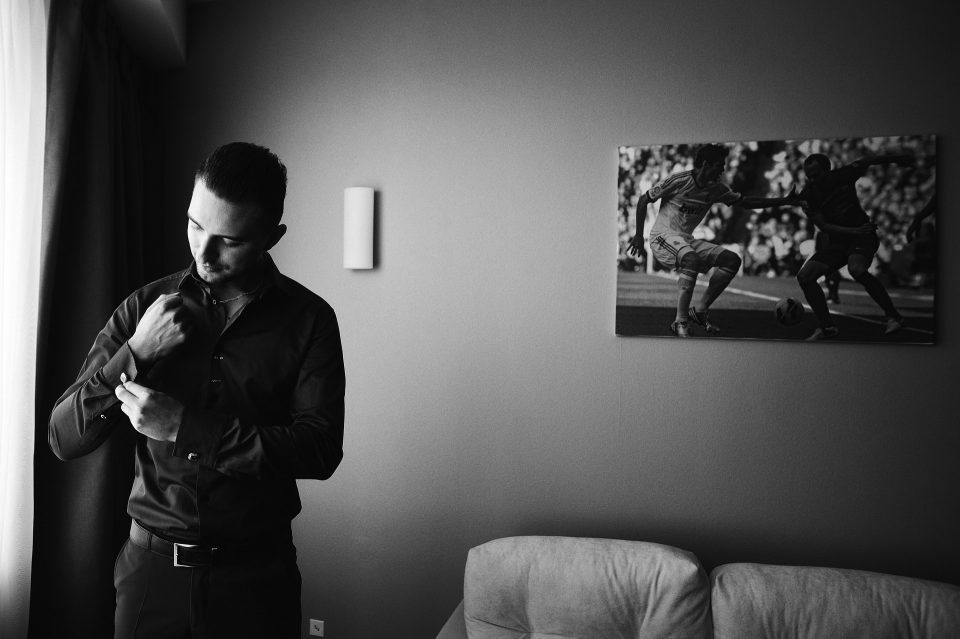 black and white photo of a man in black shirt and trousers buttoning his cuff getting the Joseph Gordon-Levitt style