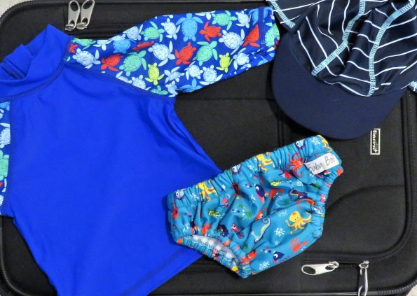 suitcase with a reusable swim nappy, a hat and a swim top on top of it