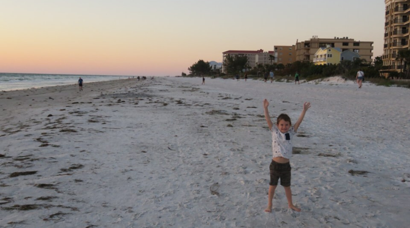 child on a beach with his arms up in the air