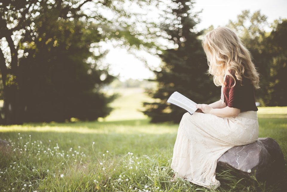 lady on a rock reading a book looks like she is having down time