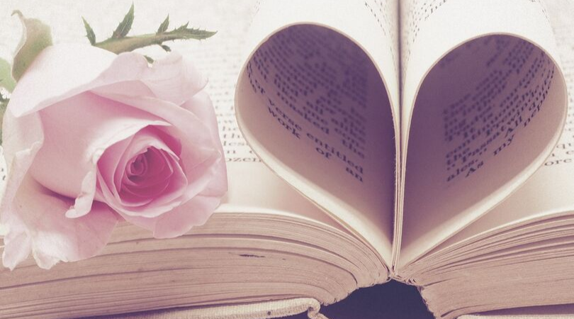 book folded into a heart shape with a rose next to it