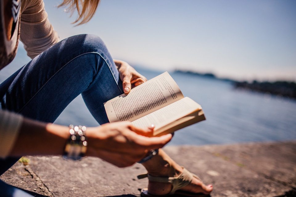 a lady reading a book next to the sea one of the positive new year's resolutions