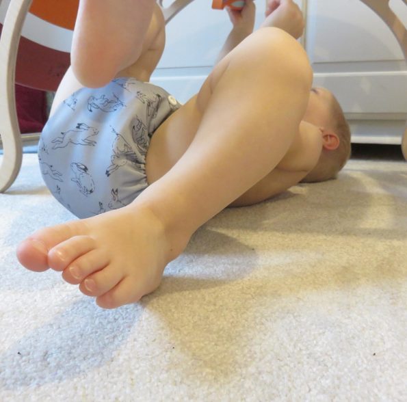 baby on his back under a wooden climber weraing a reusable nappy