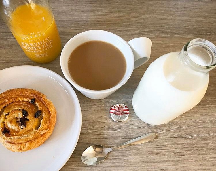 a cup of tea, pastry, milk and orange in glass bottles