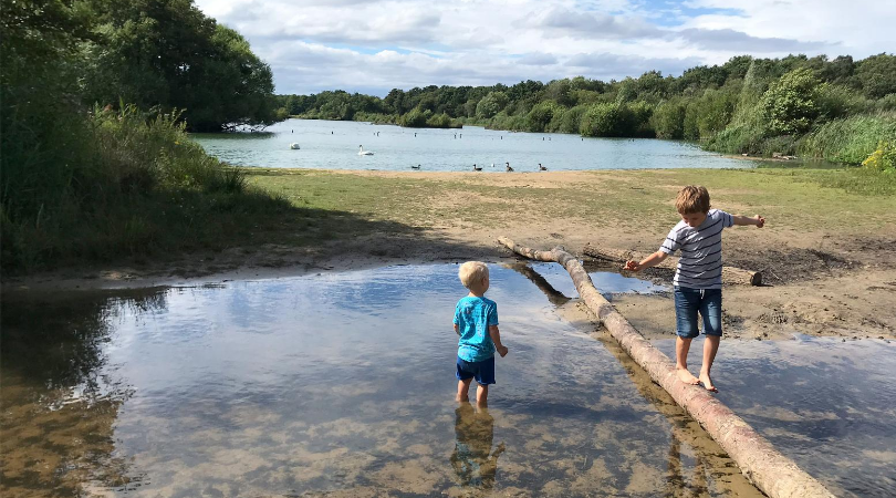 2 boys in water, one balancing on a log and the other paddling