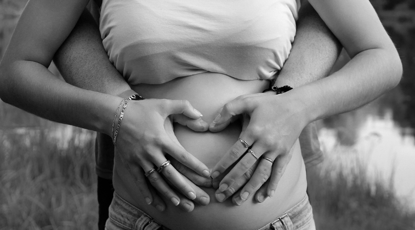 black and white photo of a man and woman holding a baby bump