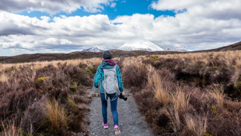 a lady hiking through a bushy field holding a camera 