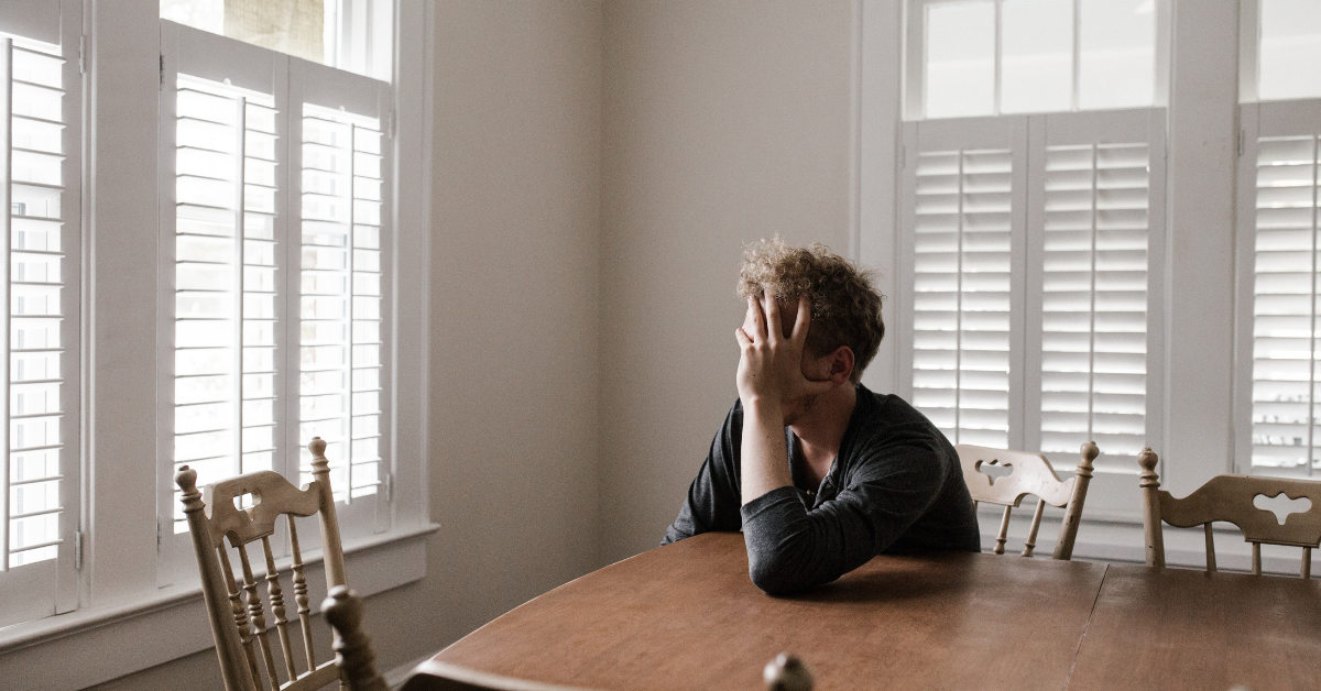 a man with his hand on his head sat at a table. Looks like he is worrying