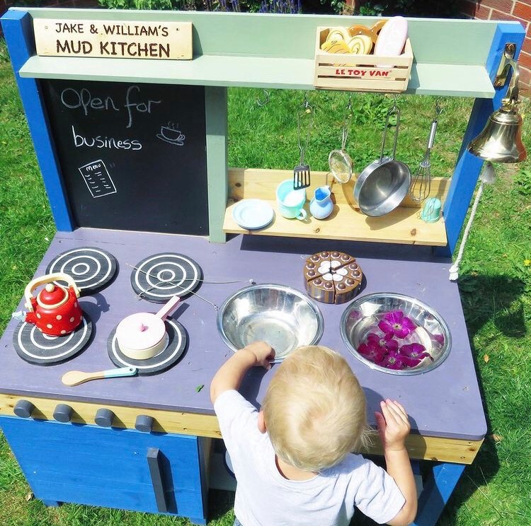 small child playing with a mud kitchen with water and petals