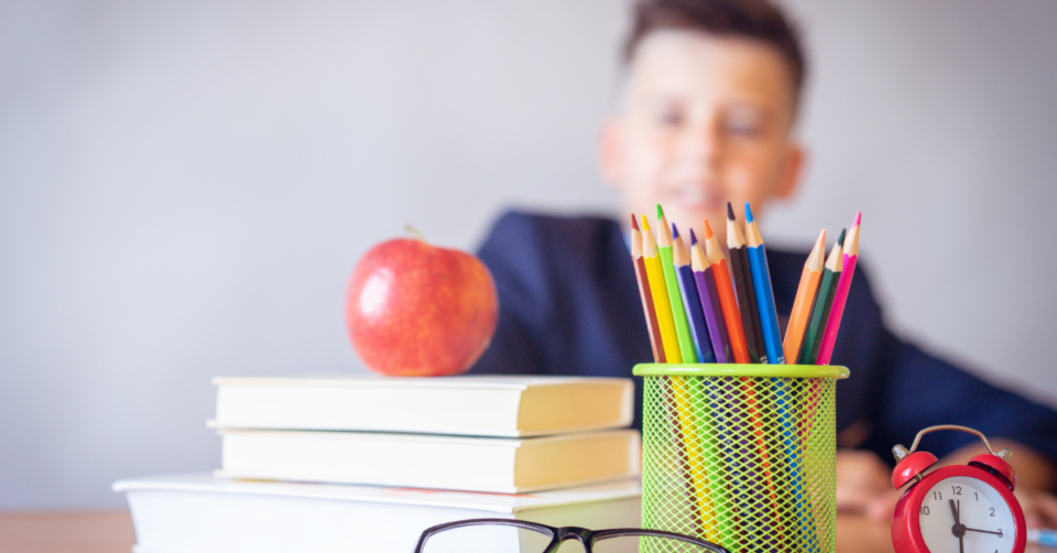 a table of school items with a child sat behind