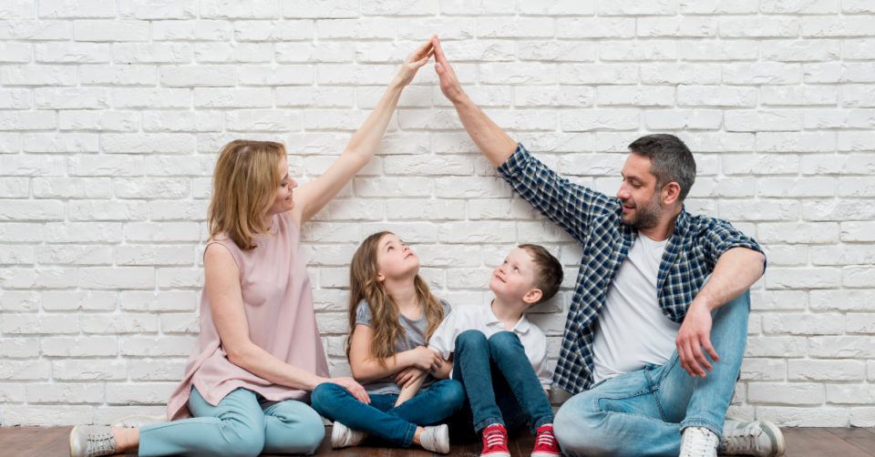 2 parents holding their hands above their 2 kids heads to make the roof of a home shape
