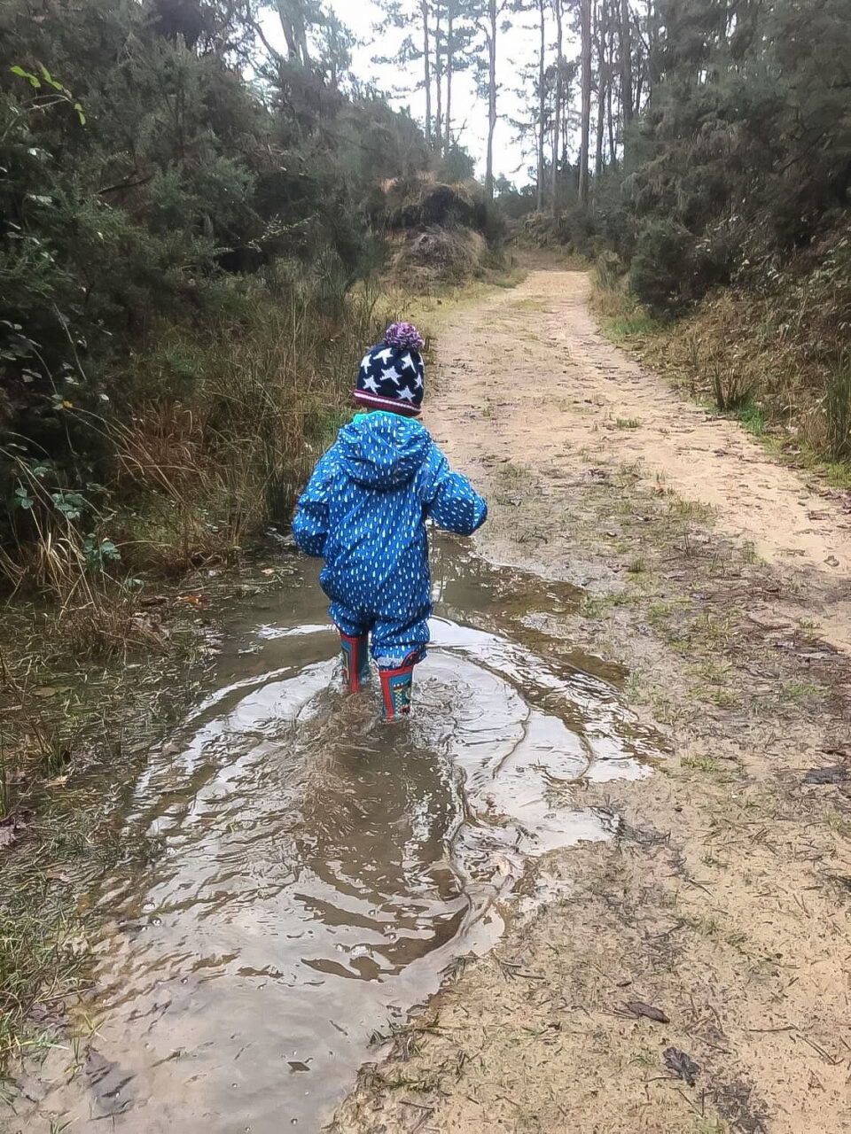 child in waterproofs and wellies walking through a puddle at Hogmoor Inclosure in Hampshire