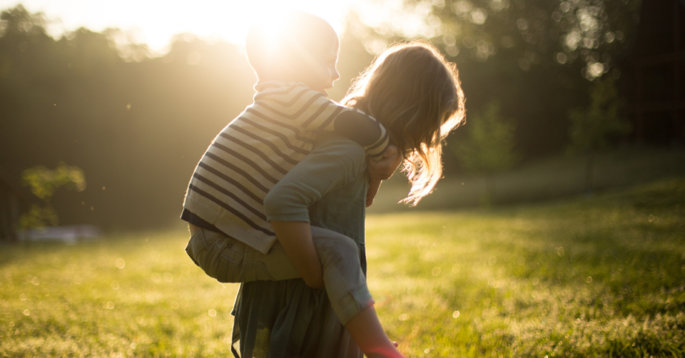 one child giving another a piggy back with the sunlight behind them at golden hour