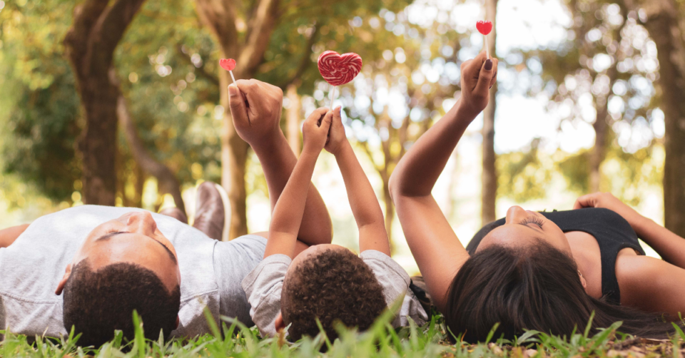 a family laying down outside holding heart shapes
