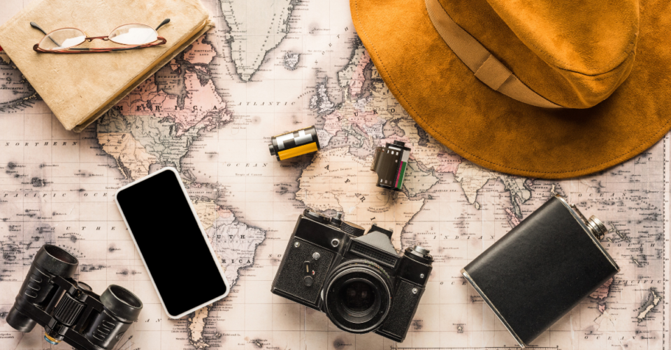 a map, camera, pjone, hat, film all laid out