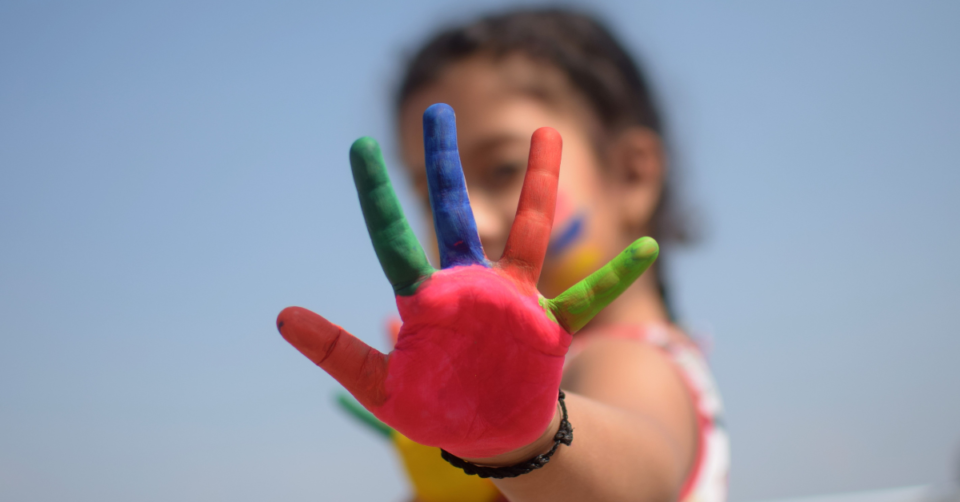 child with painted hand up with red, green and blue