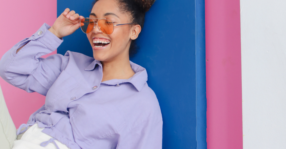 a lady laughing wearing glasses with a bright blue and pink background