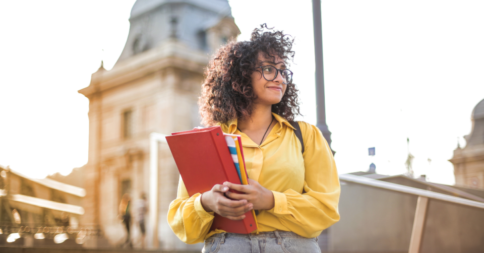 a girl holding a folder stood out side a college building