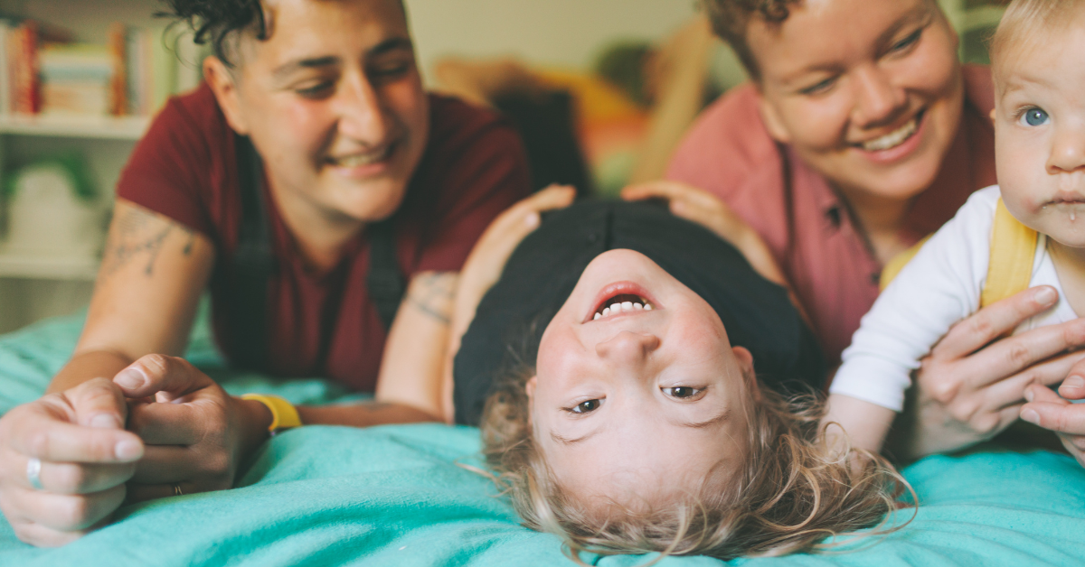 2 parents on a bed with 2 smiling kids