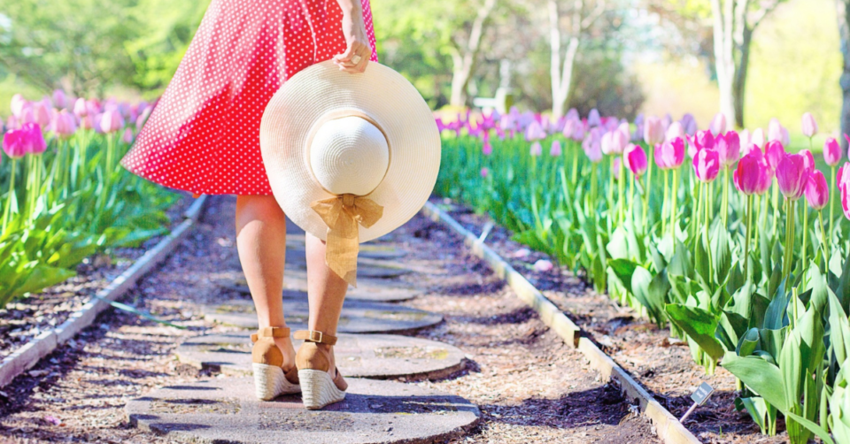 a garden path with a lady standing on stepping stones surrounded by pretty pink tulips