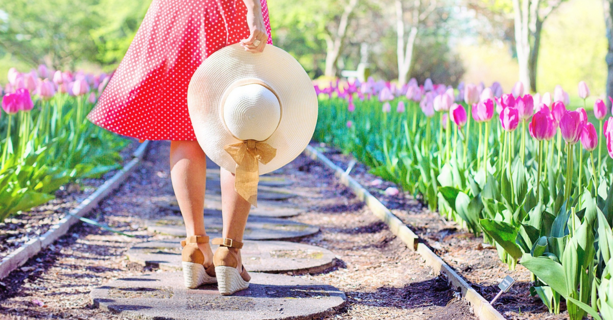 a garden path with a lady standing on stepping stones surrounded by pretty pink tulips