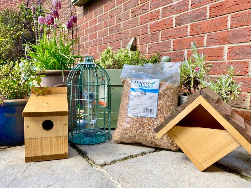 the Happy Beaks products including the multi-nester nesting box, the bird feeder, the wild bird seed mix and the Robin nesting box sat on a patio surrounded by plants in pots