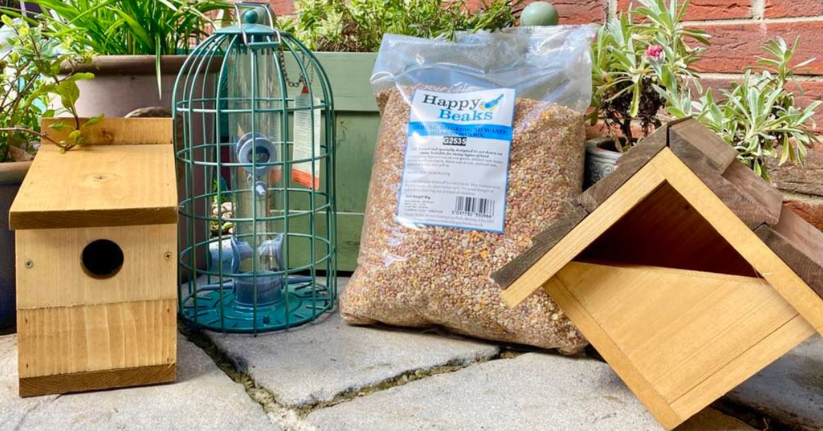 The Happy Beaks products on a patio - mulit-nesting nest box, bird feeder, wild bird seed mix and Robin nesting box