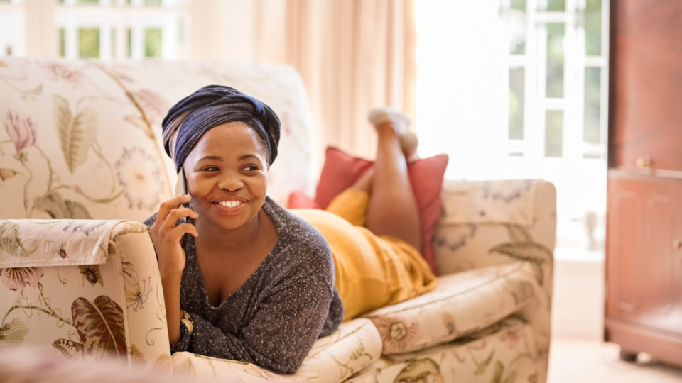 a woman smiling laying on a sofa on the phone