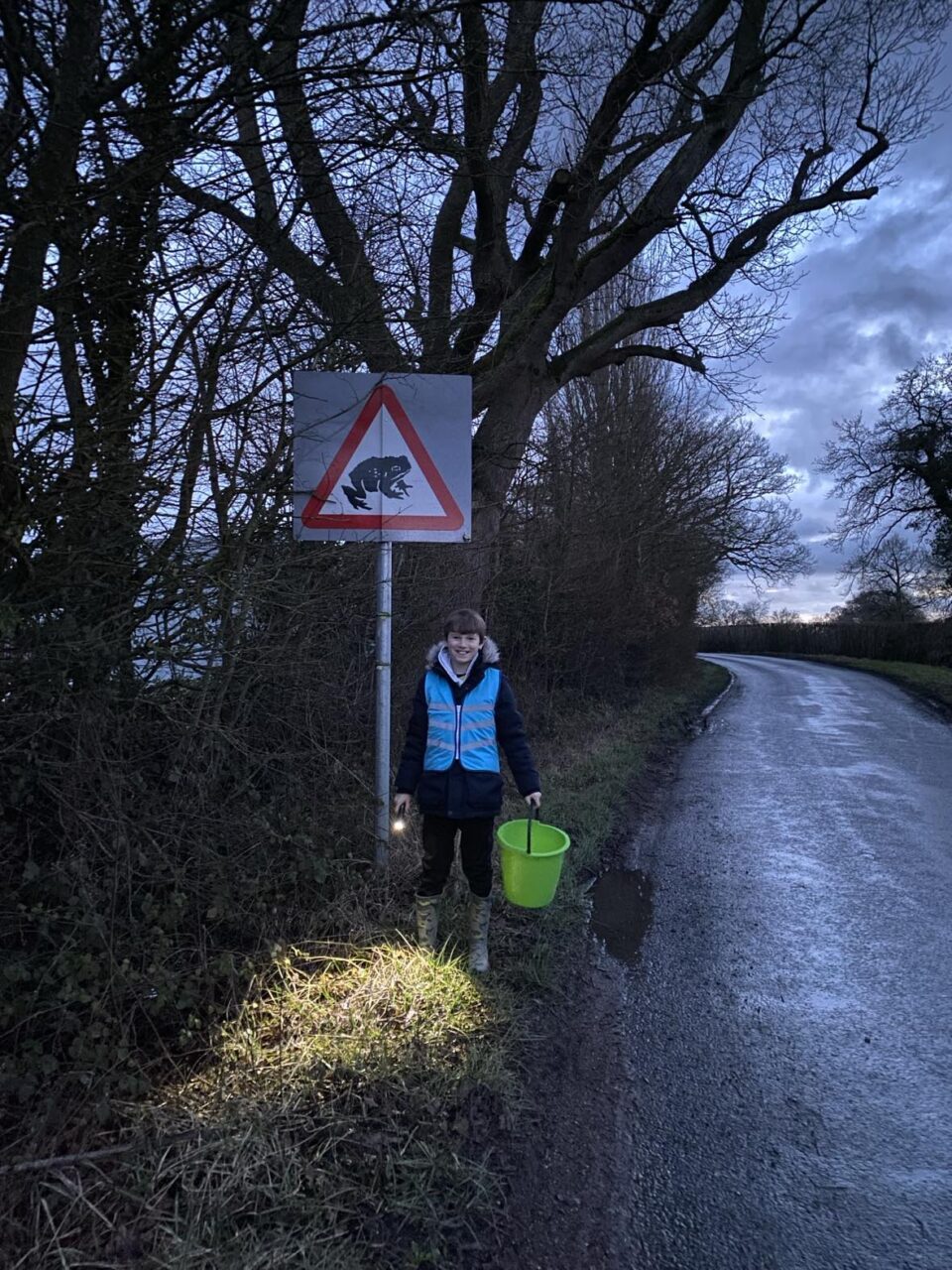 child stood by a toad warning sign on a road