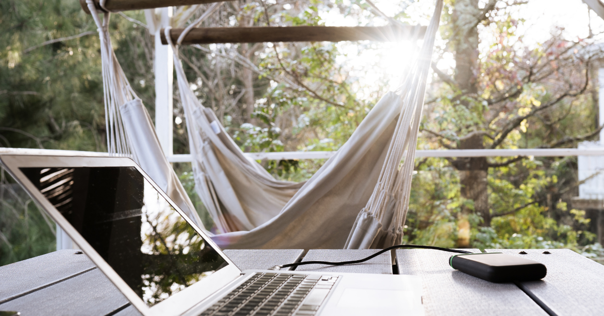 a laptop on a table with a hammock behind