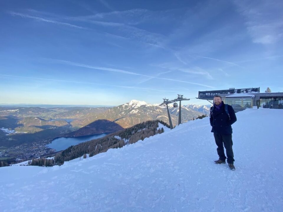 my husband at the top of the mountain with the incredible view behind him