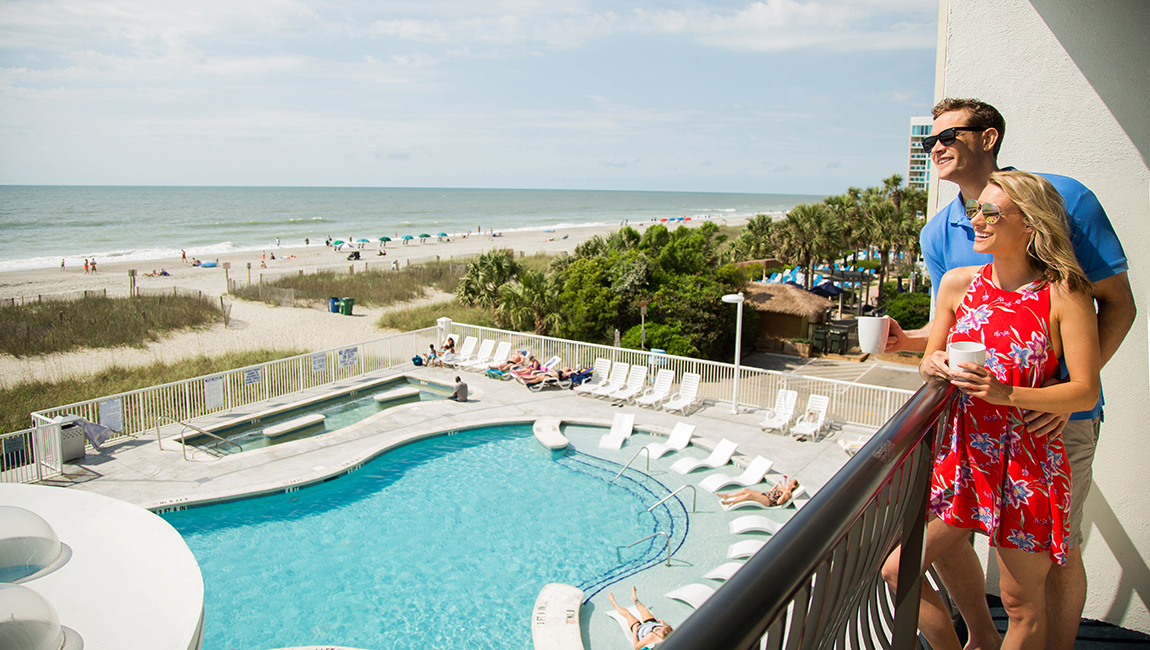 a couple on a balcony looking over a pool