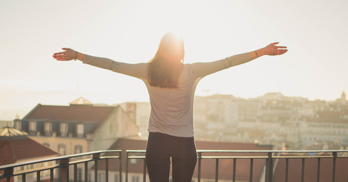 a woman on a balcony, arms outstretched in the morning