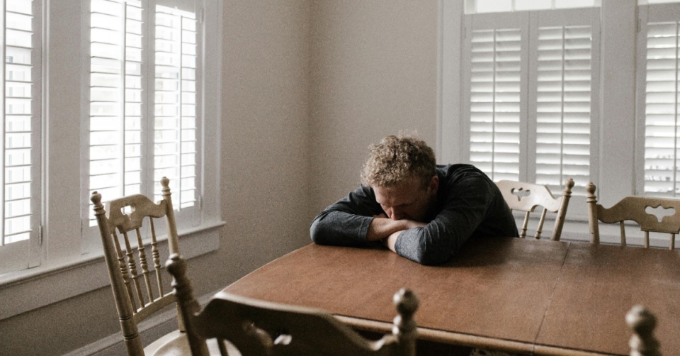 man looking sad with his head resting on his arms on a table