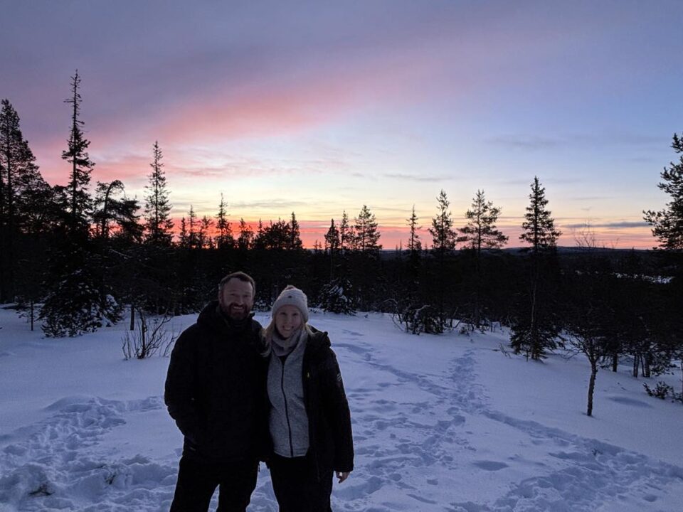 me and my husband stood in Lapland with a stunning red and purple sky behind us