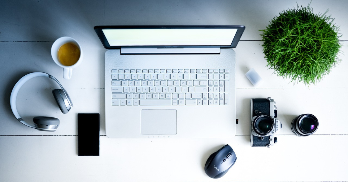 a laptop on a table with a green plant, headphones, mouse, camera and tea