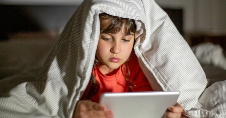 a child under a duvet looking at a tablet