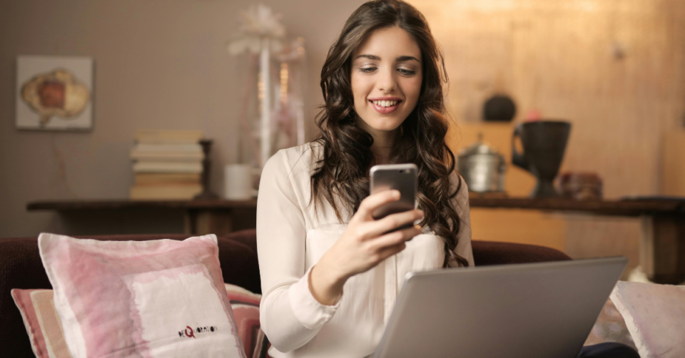 a mum working from home looking at her phone with laptop on her lap