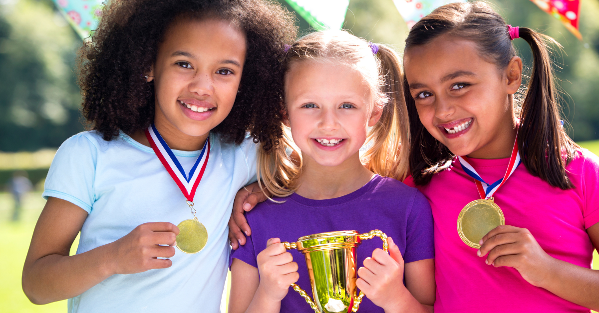 3 girls with medals and a trophy at a sports day
