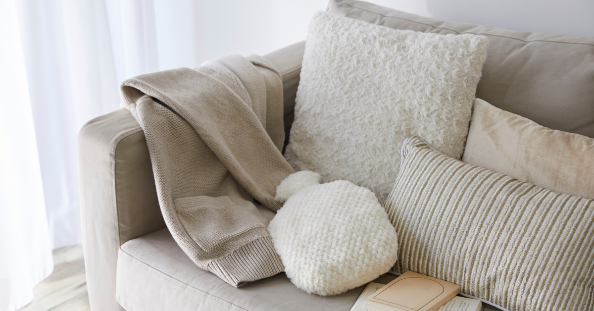 cozy items on a sofa such as cushions. throw and hot water bottle