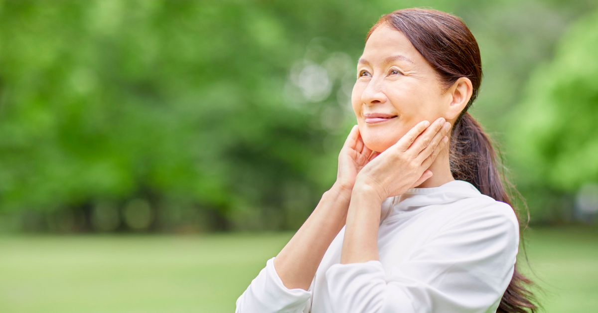 an older asian lady touching her face looking happy and healthy