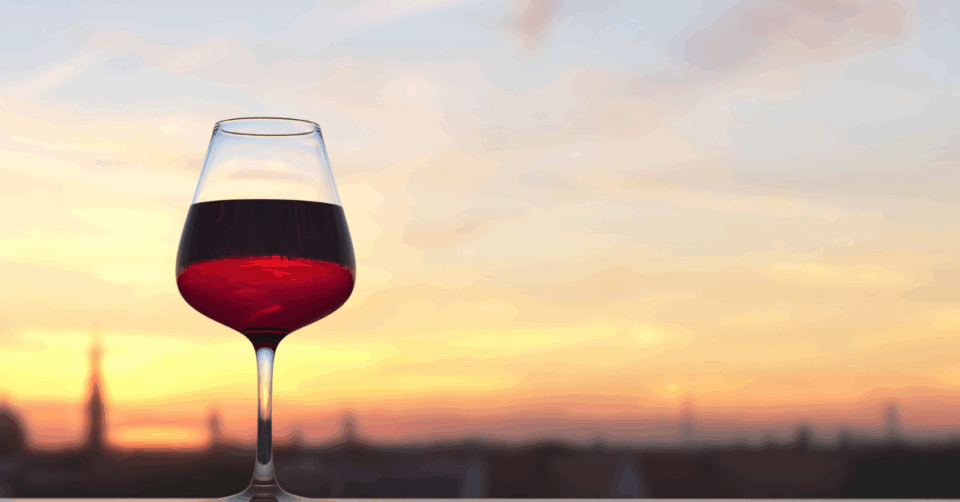 a red wine in a glass with a sunset in the background