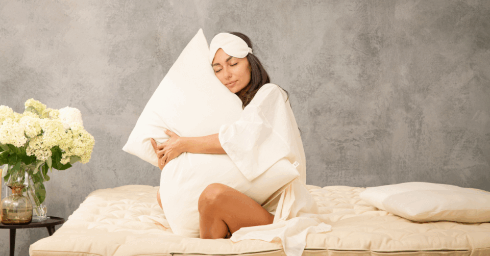 a lady hugging a pillow wearing an eye mask sat on a mattress