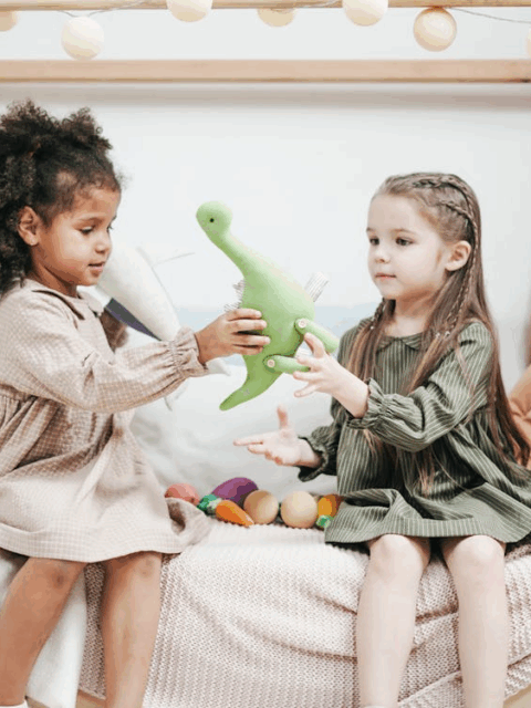 two little girls playing with a dinosaur toy